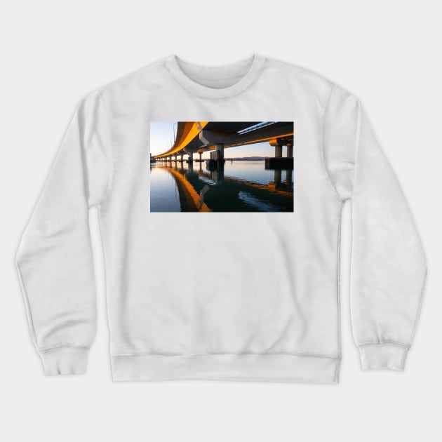 Morning sun strikes side Tauranga Harbour Bridge in golden hue reflected leading lines into calm water below Crewneck Sweatshirt by brians101